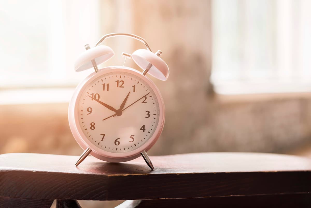 pink-alarm-clock-wooden-table-sunlight